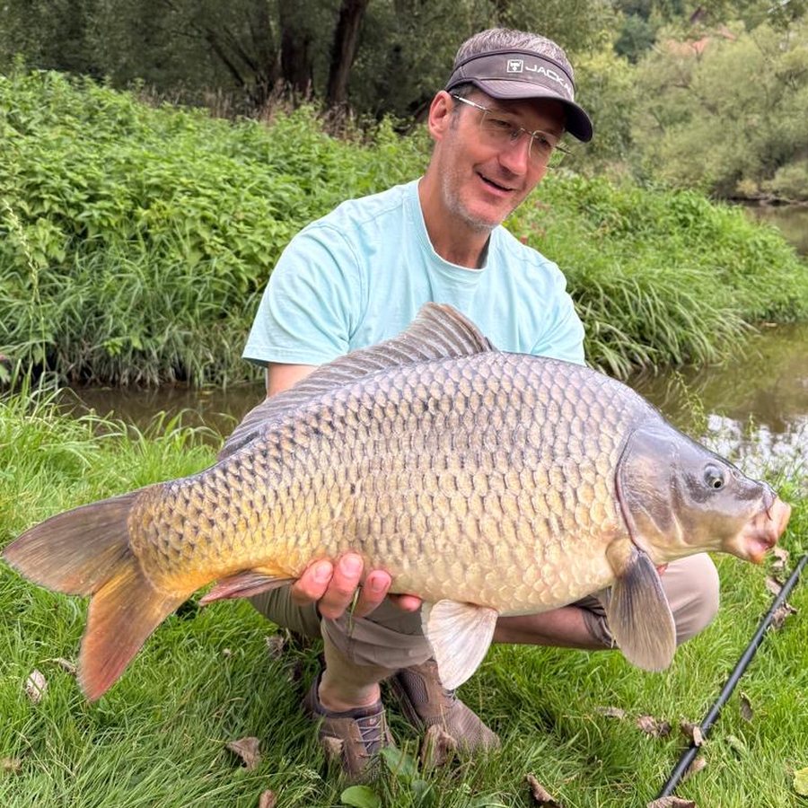 Oleg kneeling on a riverbank with a big common carp