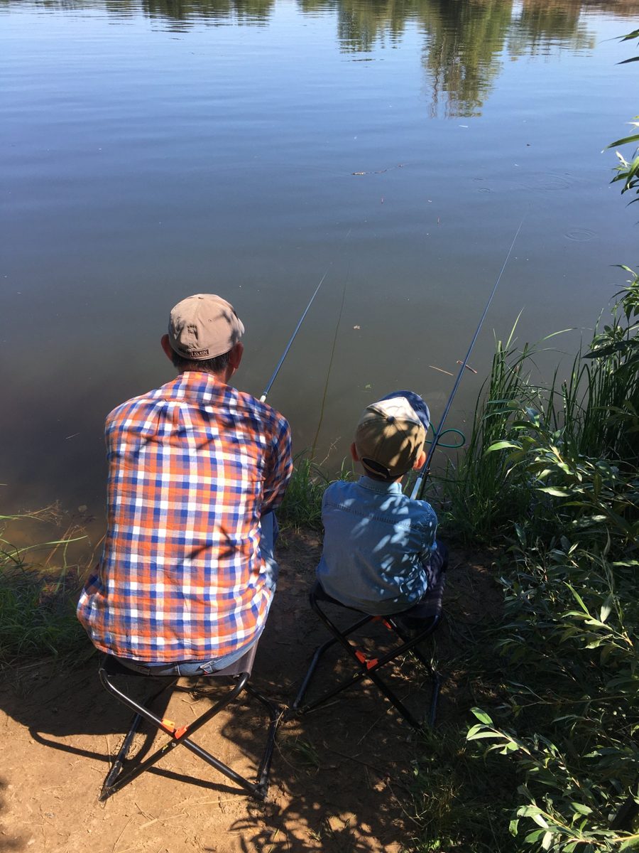 Father and young son float fishing side by side on folding stools at a calm lake