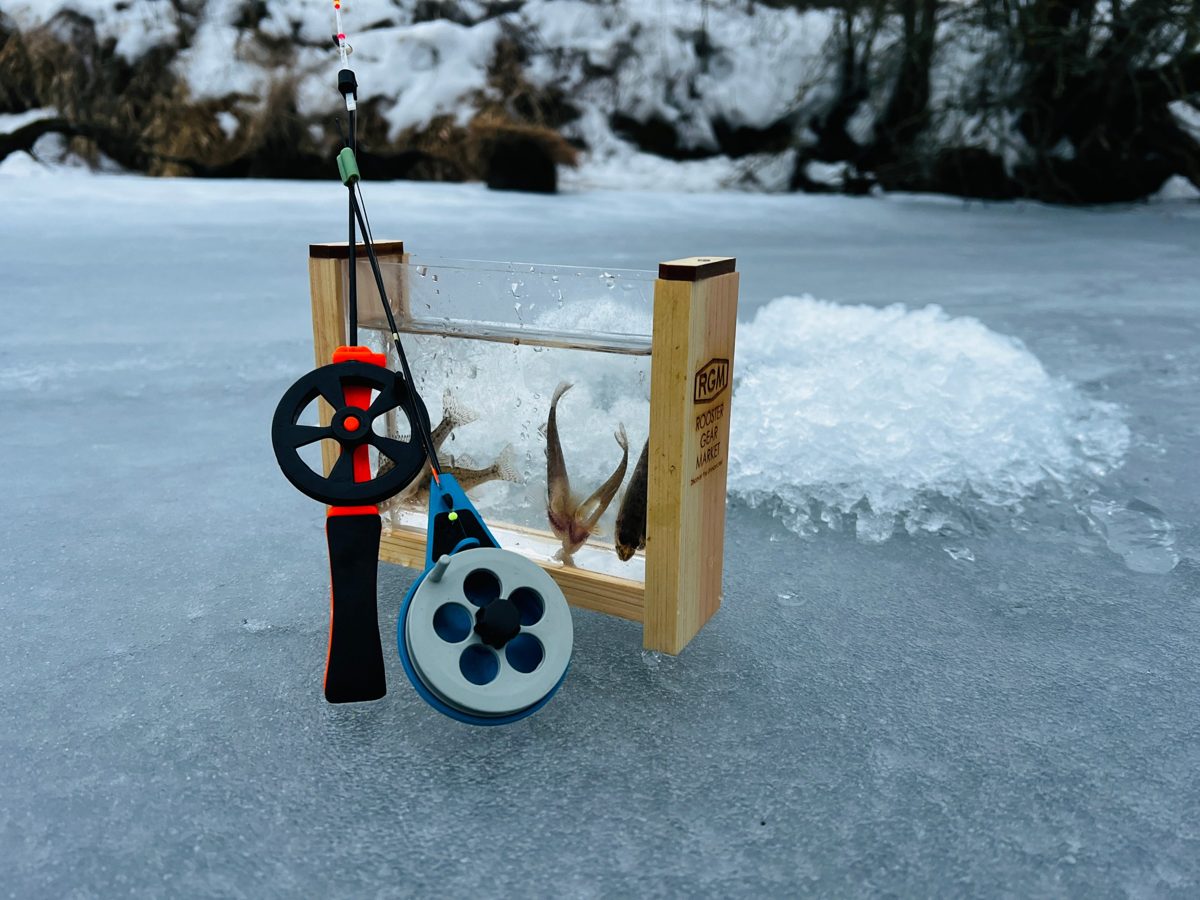 Two small ice fishing rods leaning on a box with freshly caught fish, on a frozen pond