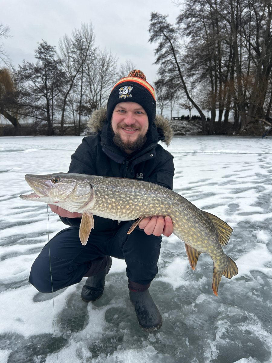 Smiling angler kneeling on a frozen lake with a big pike