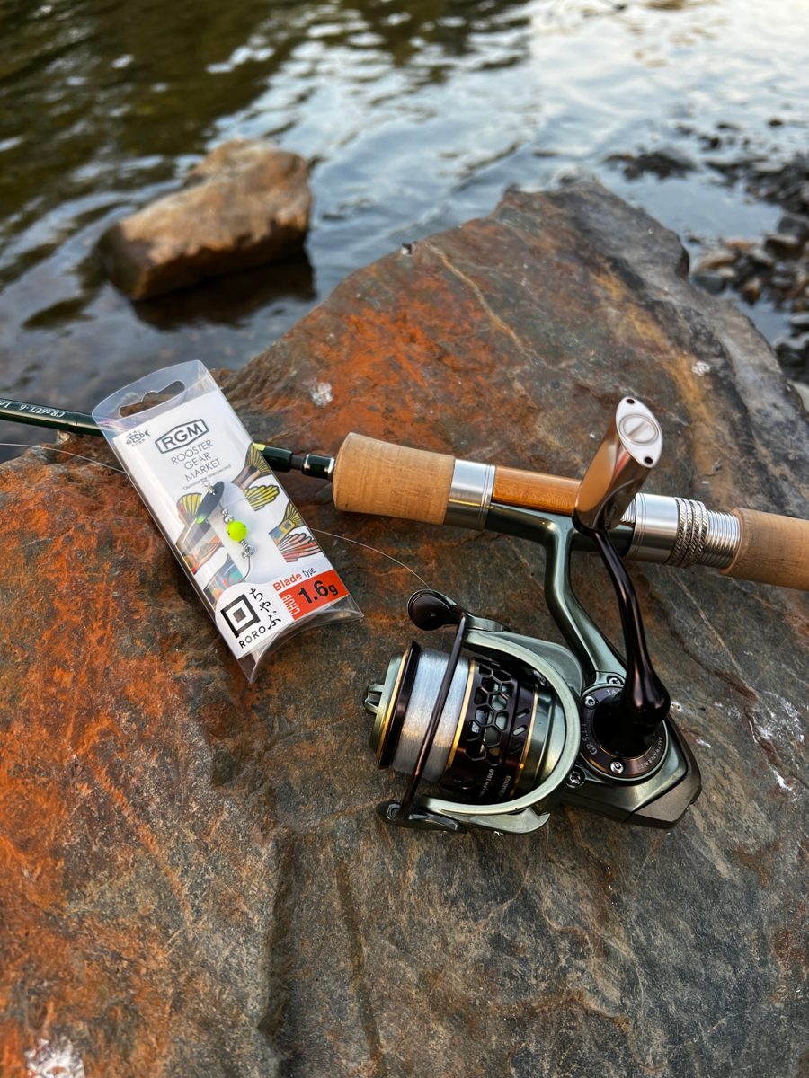 Spinning rod and reel on a riverside rock with a packet of small blade lures