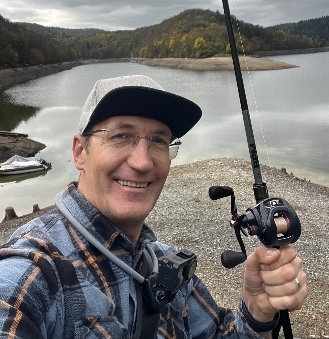 Oleg smiling with a baitcasting rod at a reservoir in autumn